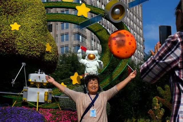 <p>A woman holds a national flag near a floral display featuring a theme of China Space Mission for the upcoming National Day celebration, in Beijing, on 23 September 2024</p>